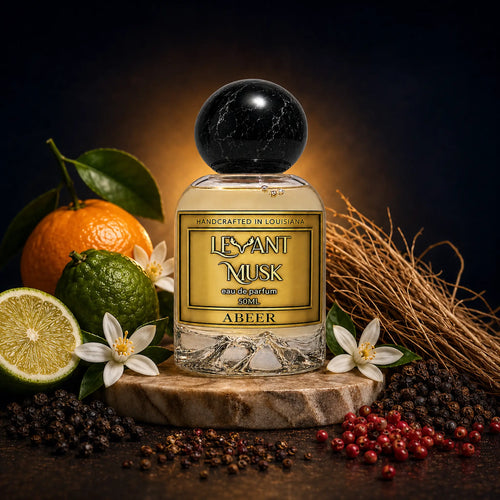 A eau de parfum bottle labeled ABEER by 'Levant Musk' with a black marble-like cap, styled on a marble pedestal with citrus fruits, flowers, dried grass, and peppercorns against a dark background.