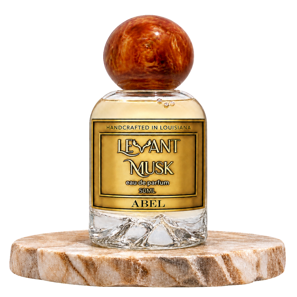A 50ml bottle of Levant Musk Eau de Parfum labeled Abel, featuring a clear glass bottle with amber-colored liquid, a gold label, and a round polished amber cap, displayed on a round marble coaster against a white background.