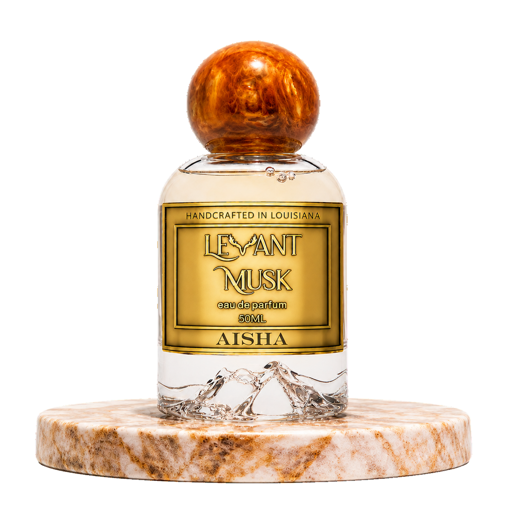 A 50ml bottle of Aisha by 'Levant Musk' eau de parfum, featuring a clear glass body with a gold label and a round, polished brown wooden cap, displayed on a marble pedestal against a white background.