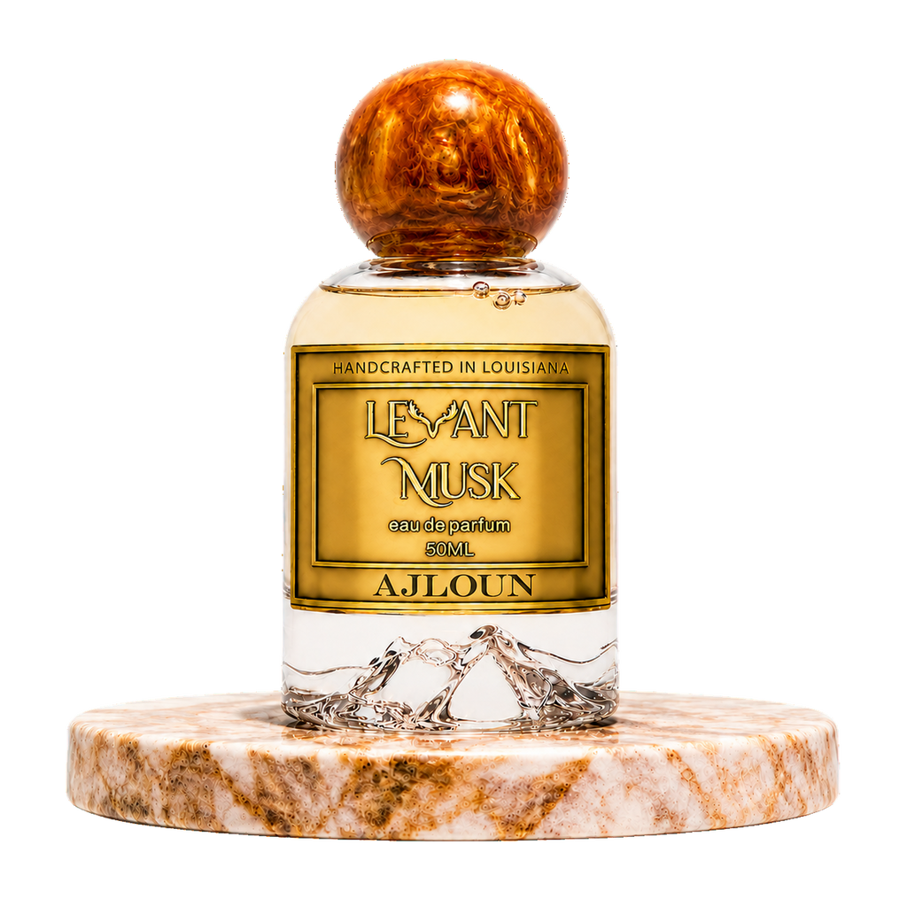 A bottle of AJLOUN eau de parfum by Levant Musk centered on a white background, resting on a round marble coaster. The bottle has a gold label with black text, a clear lower section showing water droplets, and a polished amber-brown wooden cap.