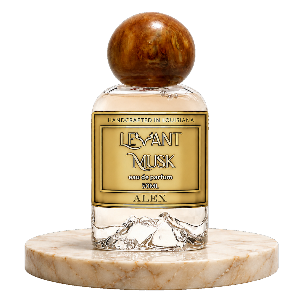 A clear glass perfume bottle with a round polished amber cap and a gold label reading ALEX,  by Levant Musk 50 ml eau de parfum', displayed on a round beige marble base against a white background.