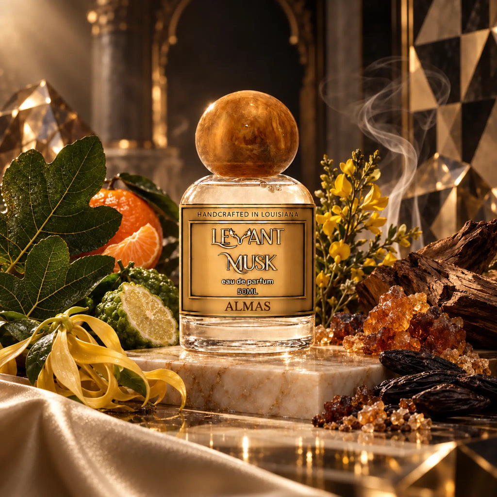 A perfume bottle labeled 'Levant Musk' eau de parfum named 'Almas' sits on a marble slab in a richly styled setting with citrus fruits, green leaves, yellow flowers, crystals, and dark wood, under warm dramatic lighting.