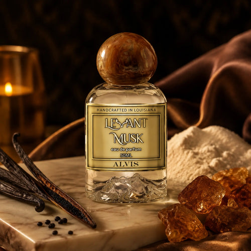 A bottle of ALVIS Levant Musk eau de parfum 50ml, featuring a clear glass bottle with a round plastic cap and a gold label, styled on a marble slab with vanilla beans, amber crystals, and a lit candle in the background.