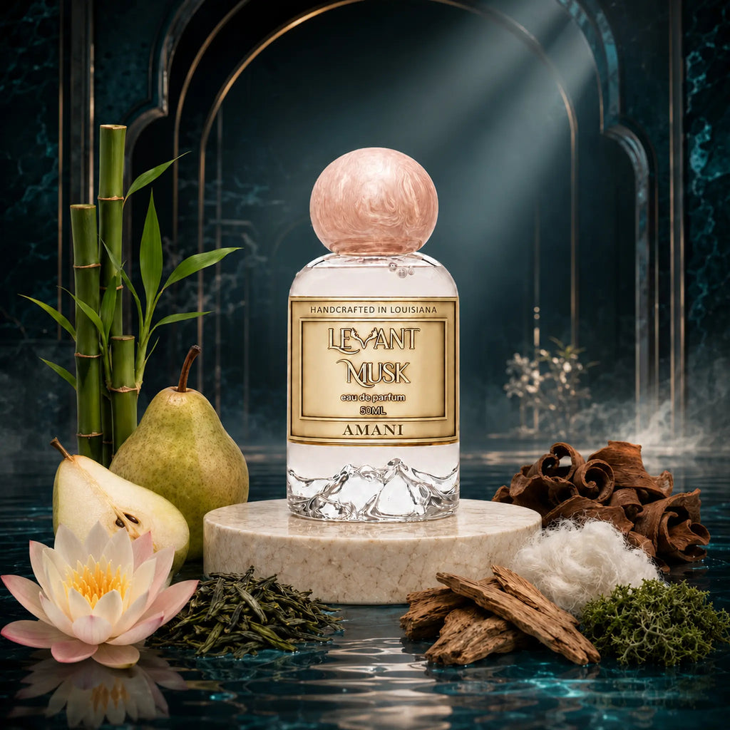 A perfume bottle labeled Amani, by Levant Musk eau de parfum displayed on a marble pedestal with botanical and spice props including a pear, lotus flower, cinnamon, and tea leaves against a dark arched backdrop.