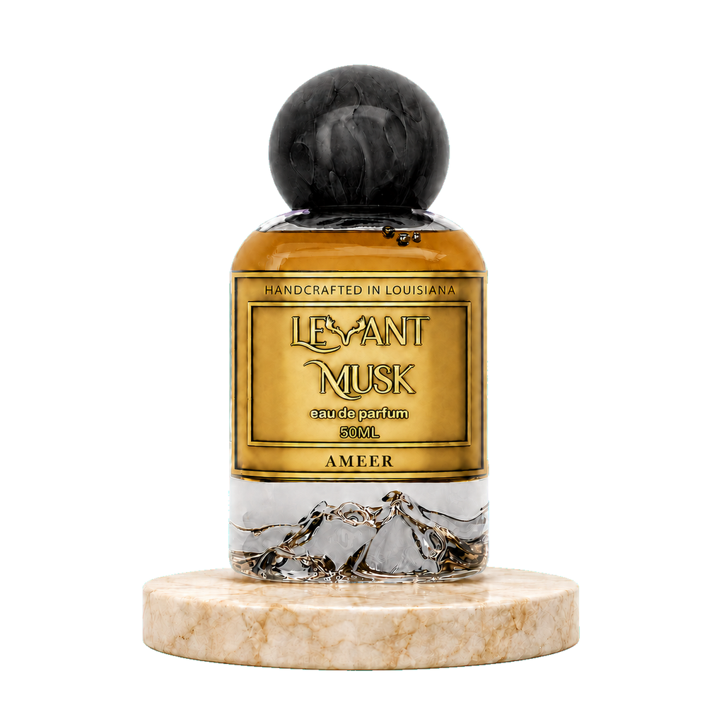 A 50mL bottle of Ameer by Levant Musk Eau de Parfum, featuring amber liquid, a gold label with black lettering, a black marble sphere cap, and a clear lower section showing gold mountain illustrations. The bottle is displayed on a round beige marble base against a solid white background.