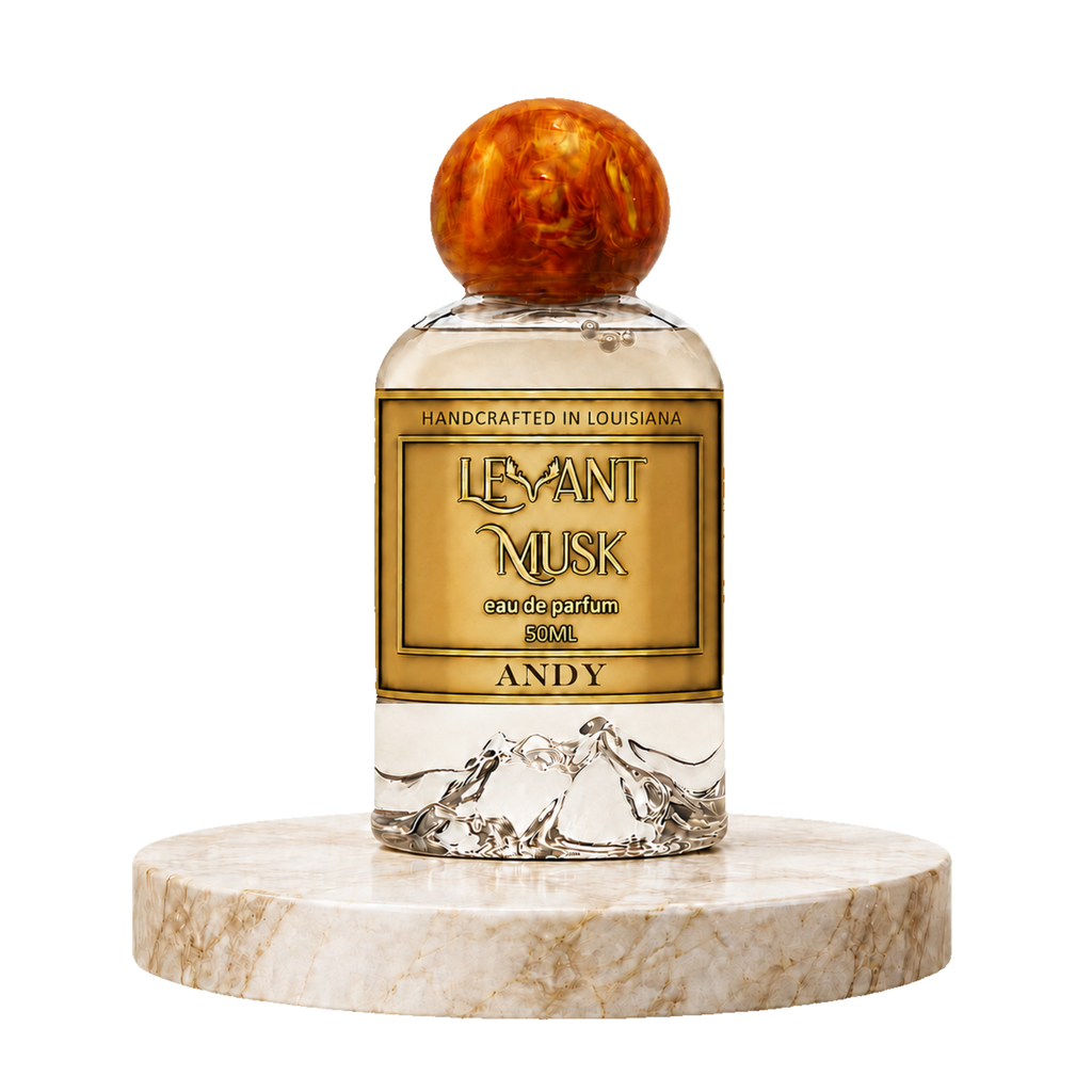 A clear glass perfume bottle with a round amber-brown cap, featuring a gold label that reads  'ANDY' eau da parfum by Levant Musk. The bottle is displayed on a round beige marble pedestal against a solid white background.