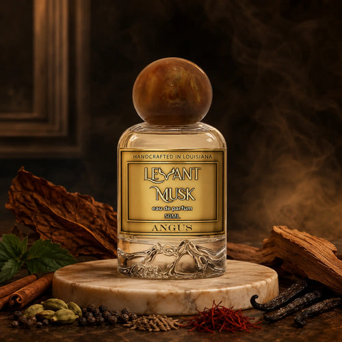 A bottle of 'Angus' eau de parfum by Levant Musk, featuring a round amber cap and a gold label, displayed on a marble slab with various spices and wood pieces against a dark, atmospheric background.