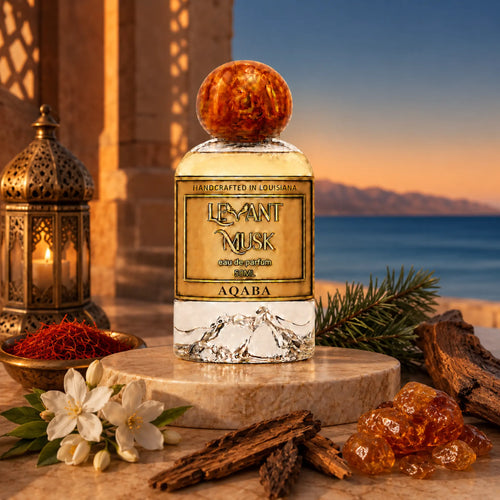A perfume bottle labeled Aqaba, by Levant Musk styled on a stone pedestal with saffron, jasmine flowers, cinnamon sticks, amber crystals, and a lantern against a sunset seascape background.