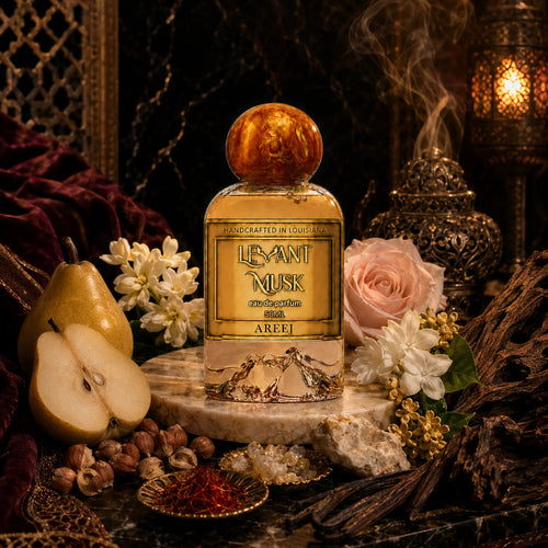 A perfume bottle labeled AREEJ, by Levant Musk, Monroe, LA styled in a rich, dark, luxurious setting with a pear, white flowers, a pink rose, hazelnuts, and a burning incense burner in the background.