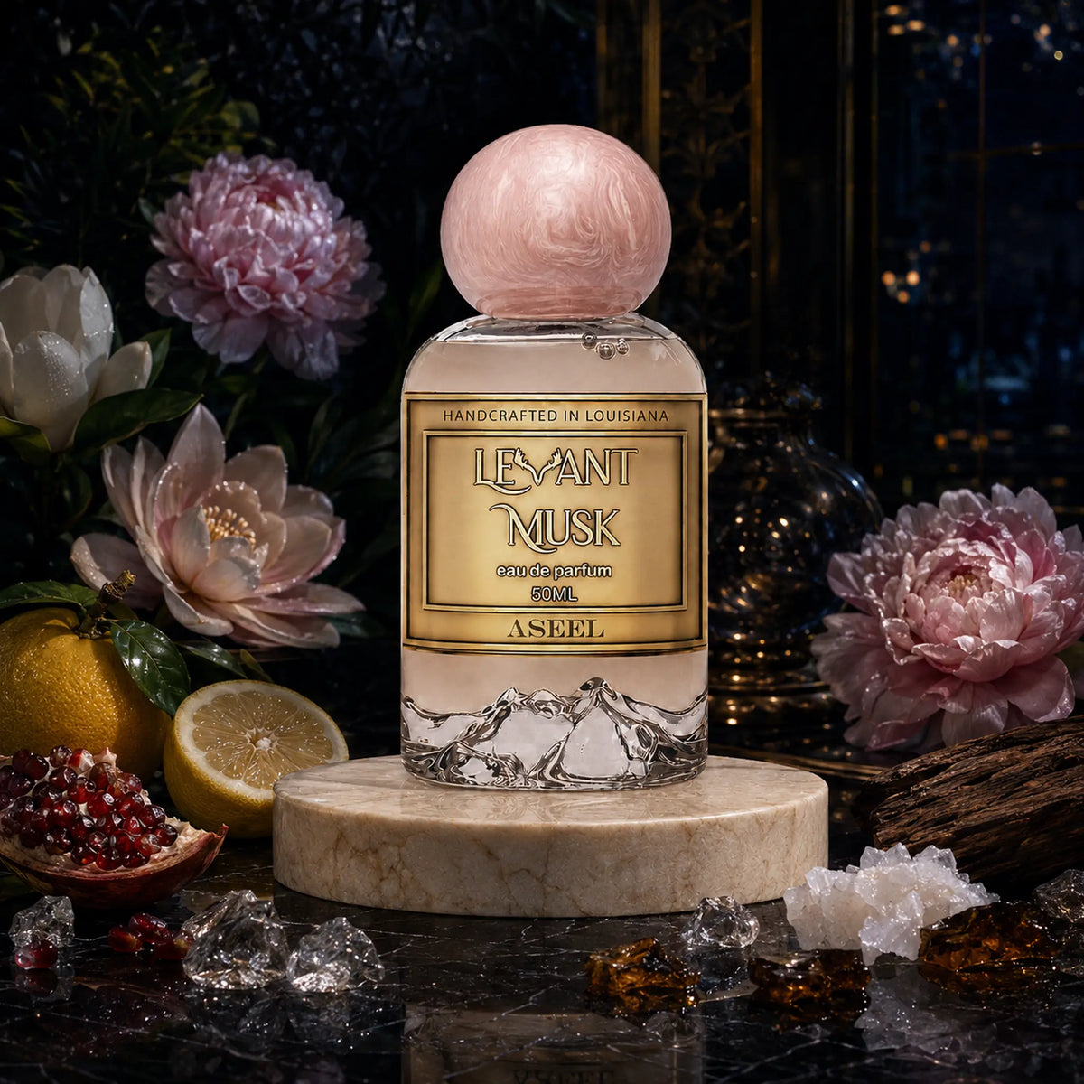 A bottle of Aseel Levant Musk cologne is centered on a marble pedestal, surrounded by pink peony flowers, lemons, crystals, and amber pieces on a dark marble surface.