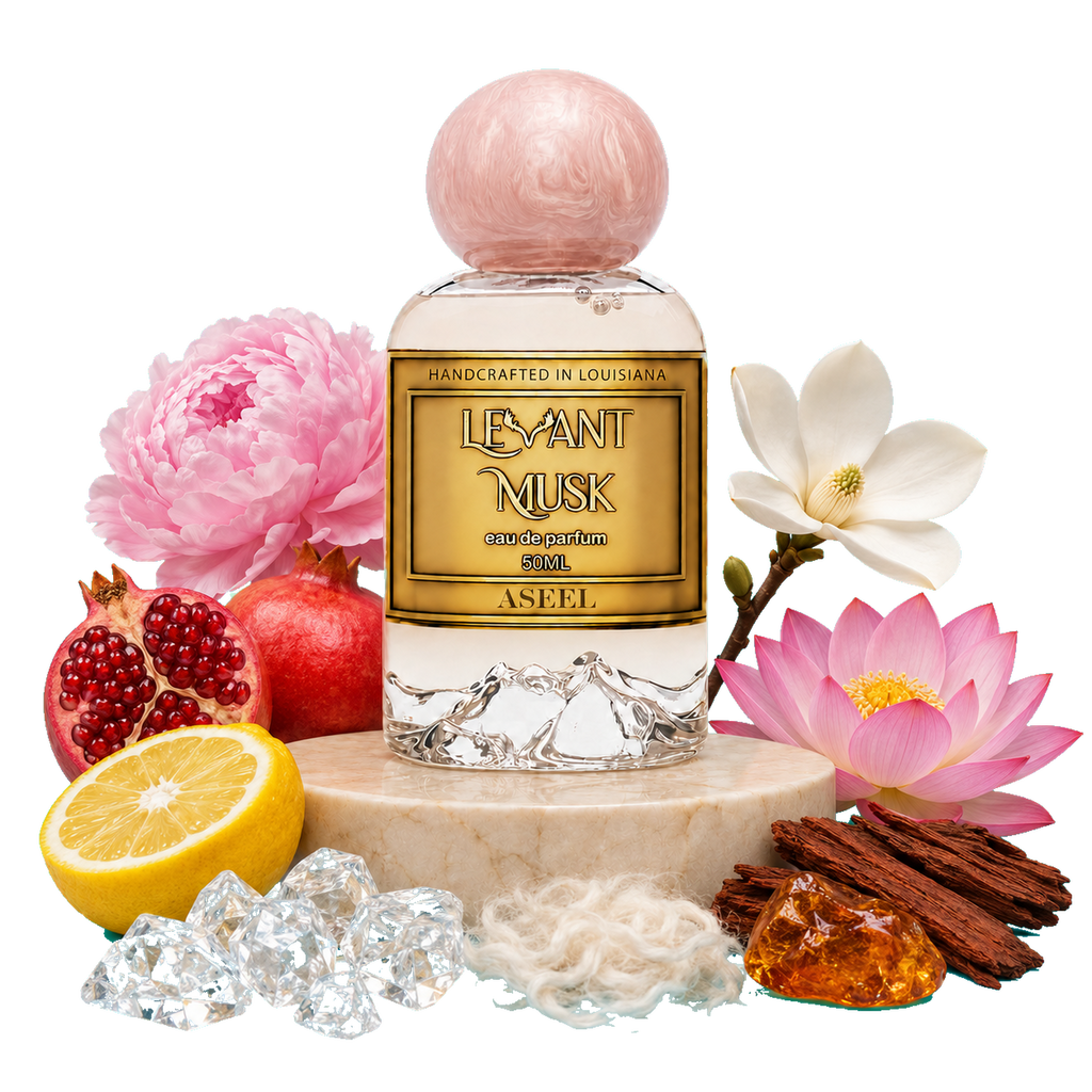 A bottle of Aseel, by Levant Musk, Monroe, LA styled with its scent ingredients including pink flowers, pomegranate, lemon, cinnamon, and crystals on a marble pedestal against a white background.
