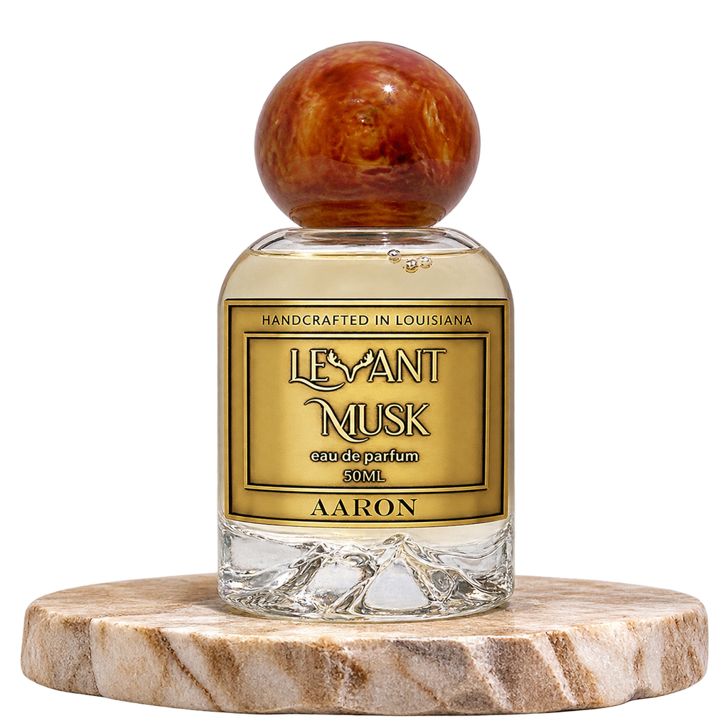 A bottle of Levant Musk Eau de Parfum labeled Aaron, featuring a clear glass bottle with a round amber-brown wooden cap and a gold label, displayed on a round marble coaster against a white background.