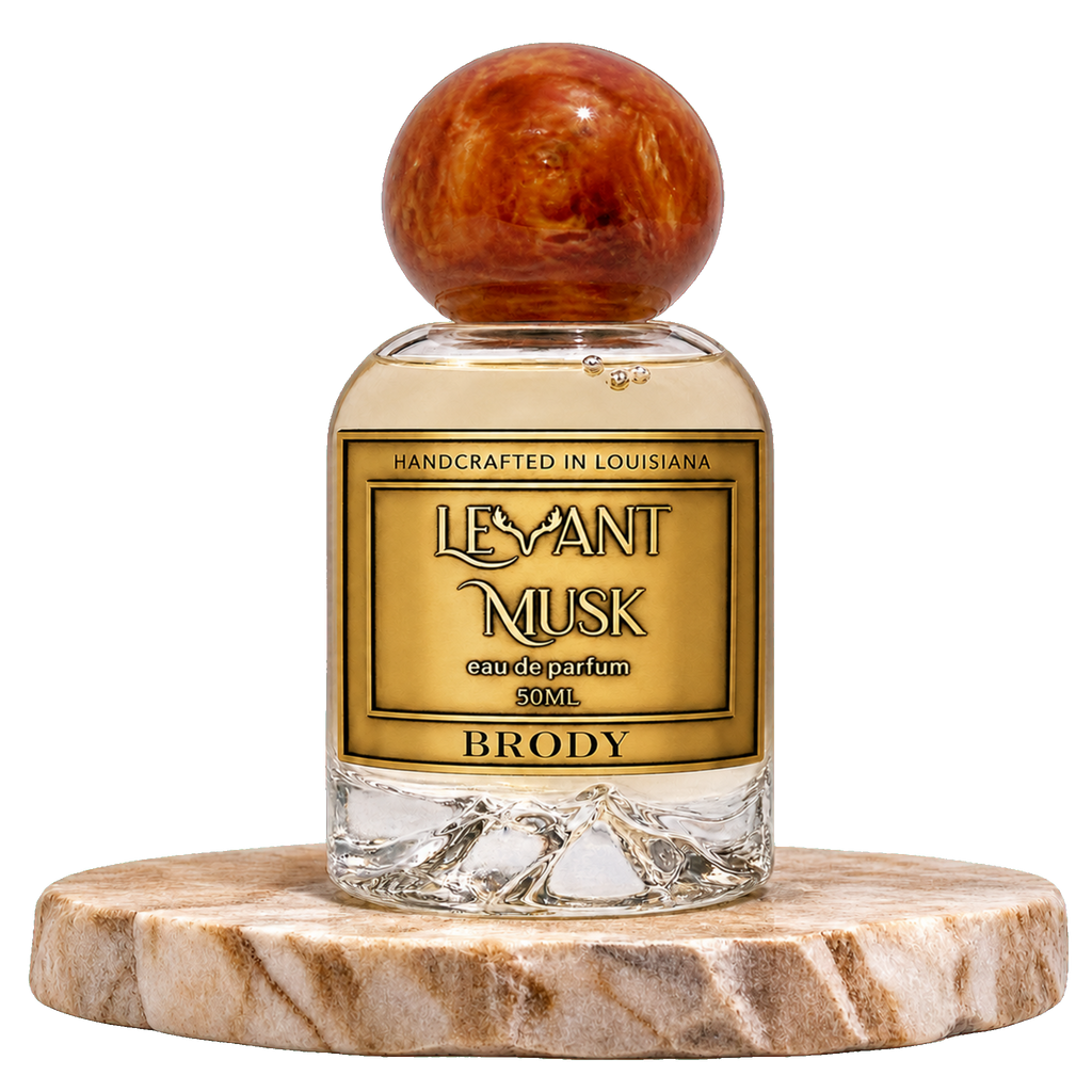 A 50ml bottle of Eau de Parfum  Brody, by Levant Musk featuring a clear glass bottle with a round, polished reddish-brown wooden cap and a gold label. The bottle is displayed on a round, polished marble coaster against a solid white background.