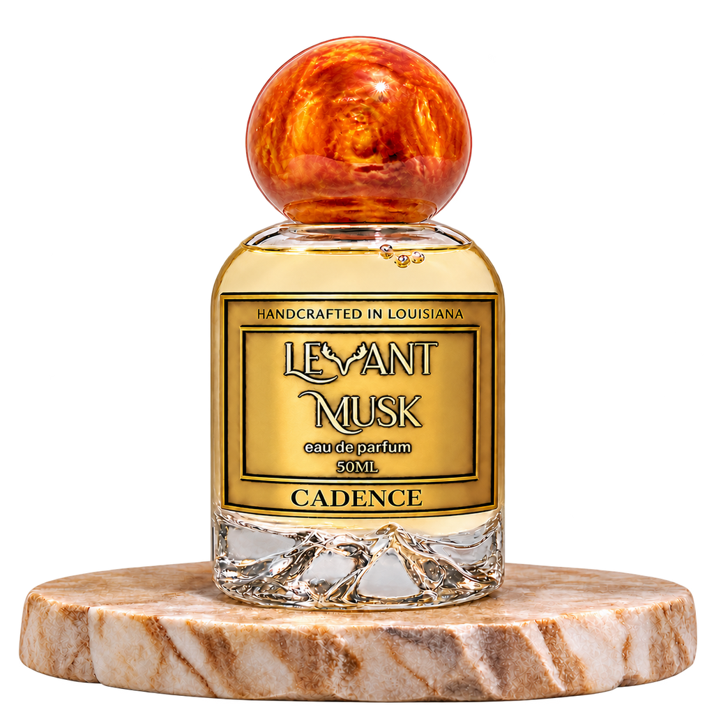CADENCE unisex eau de parfum in the Levant Musk gold-label bottle with an orange-gold spherical cap on a marble pedestal; transparent background.