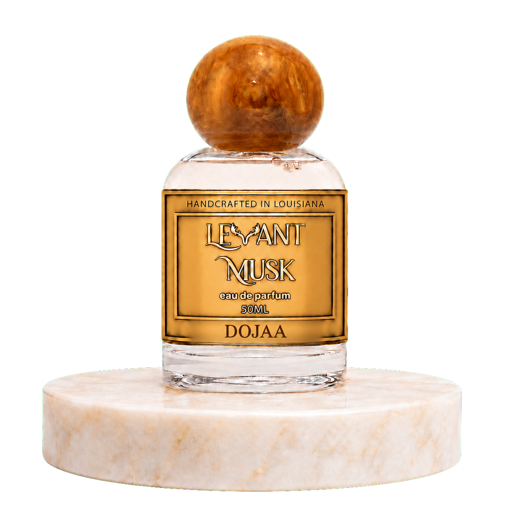 A 50ml bottle of Dojaa 'Levant Musk' eau de parfum , featuring a clear glass bottle with a gold label and a round amber cap, displayed on a white marble pedestal against a white background.