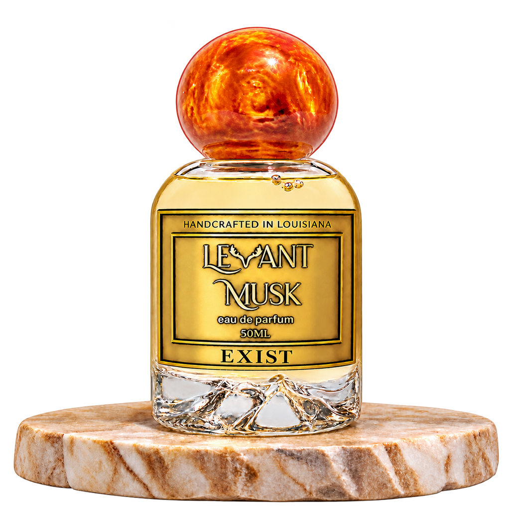 EXIST by Levant Musk, round 50 mL Eau de Parfum bottle with orange-gold marbled cap and gold label on a cream marble pedestal; transparent background.