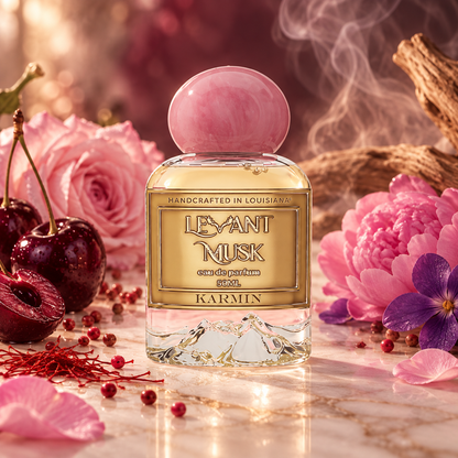 A perfume bottle labeled Karmin by Levant Musk styled with pink flowers, cherries, and red berries on a marble surface with a smoky, warm background.
