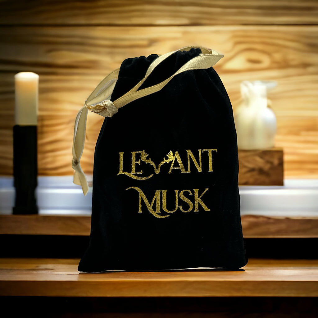 Black Levant Musk drawstring pouch with gold embroidered lettering and a gold ribbon on a wooden counter.