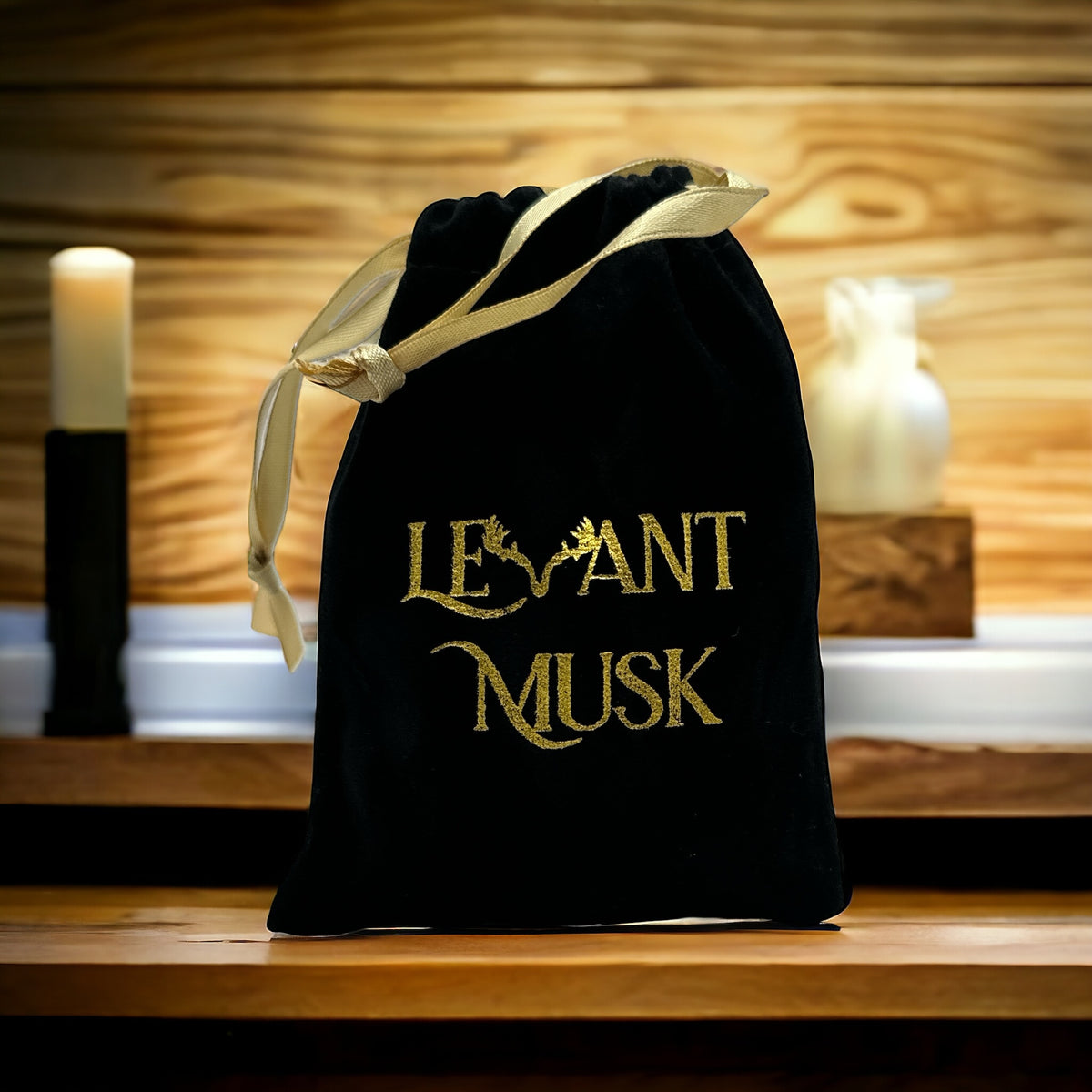 Black Levant Musk drawstring pouch with gold embroidered lettering and a gold ribbon on a wooden counter.