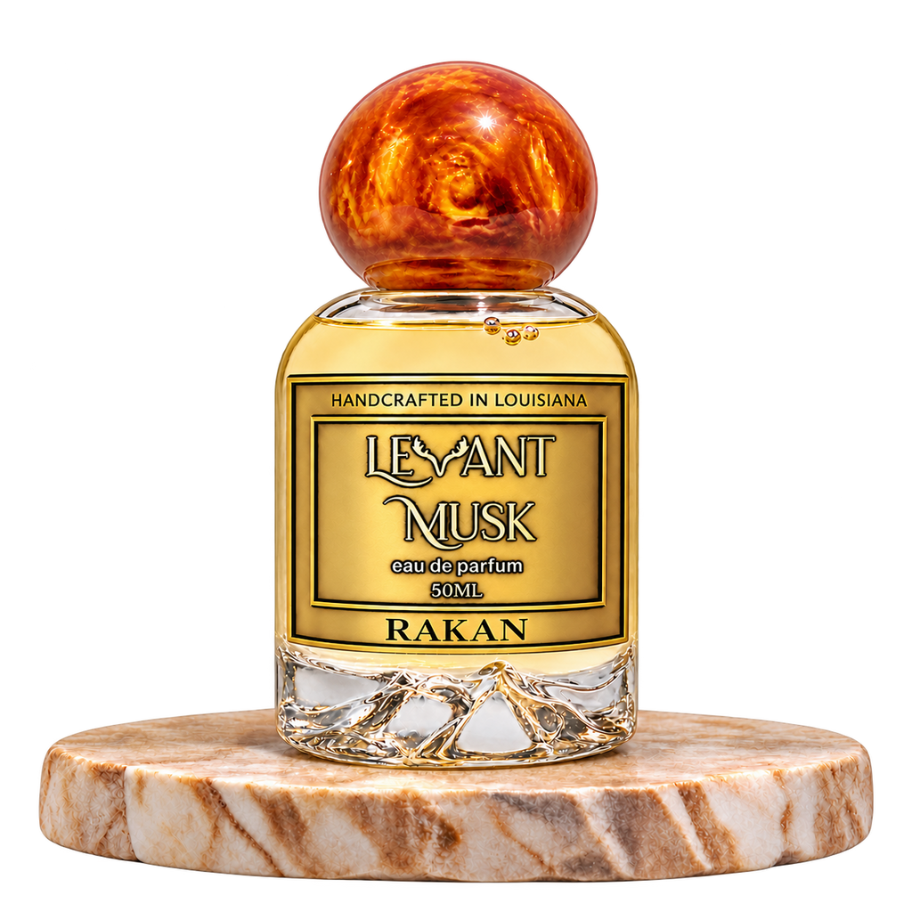 RAKAN by Levant Musk, 50 mL eau de parfum with a orange-gold marble cap on a cream marble plinth, transparent background.