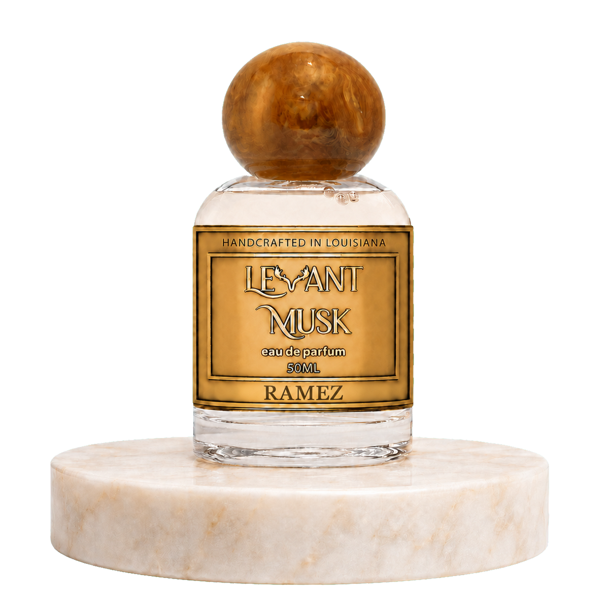 A bottle of Ramez by'Levant Musk' handcrafted perfume, featuring a clear glass bottle with a round polished amber cap and a gold label, displayed on a white marble pedestal against a white background.