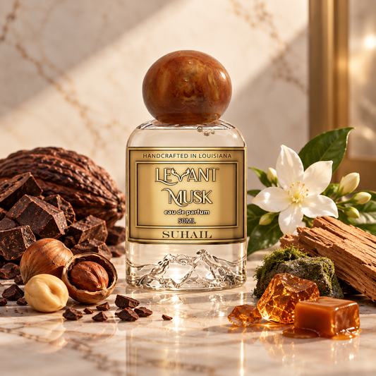 A bottle of LEYANT MUSK cologne by SUHAIL, styled with chocolate pieces, hazelnuts, a white flower, and amber honey on a marble surface.